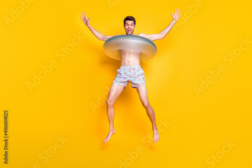 Photo of impressed funny young guy shirtless wear dark glasses smiling jumping inside water circle isolated yellow color background