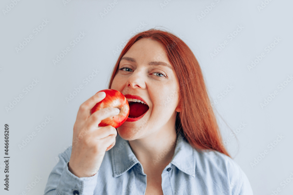 Portrait of cheerful young woman eating red apple on gray wall background. Healthy nutrition diet. Apple vitamin snack. Portrait of cheerful young woman eating red apple on gray wall background. Healthy nutrition diet. Apple vitamin snack.