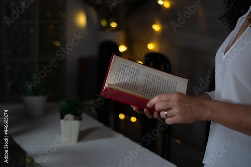 Mujer leyendo un libro rojo con fondo de luces difuminado. Woman reading a red book with blurred lights background.