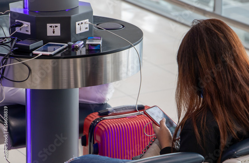 A young woman sitting at a charging station and looking at her smartphone. Recharging mobile phones from free charge station at the airport. photo