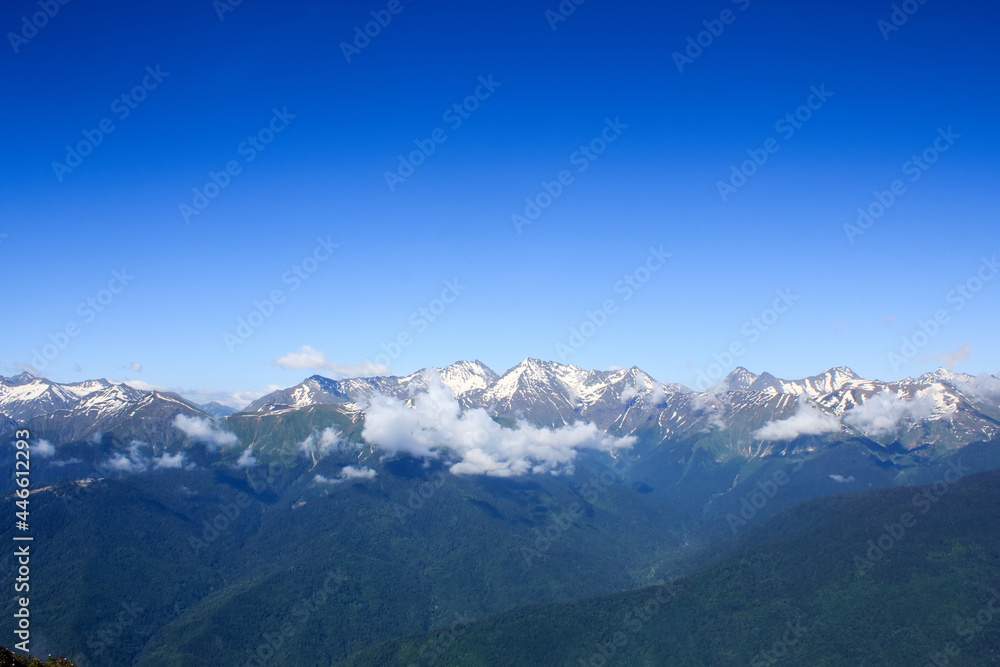 valley with forrest in caucasus mountains covered with snow under the blue sky