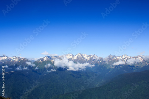 valley with forrest in caucasus mountains covered with snow under the blue sky
