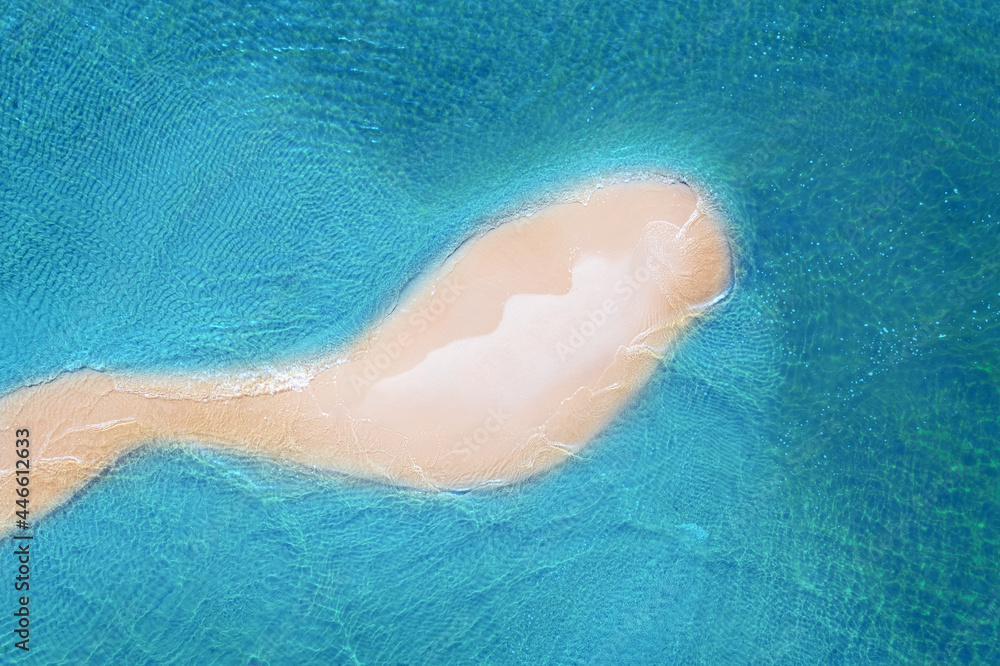 Aerial view of the sandy beach island in the transparent blue sea with waves. Summer vacation. Tropical landscape with white sand and ocean. Top view.