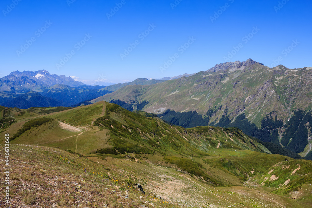 Fototapeta premium landscape with footpath in alpine meadows and high rocky mountains covered with snow
