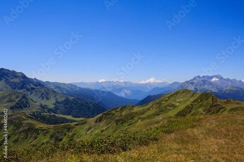 landscape of blue sky and green grass of alpine meadows with rocky mountains valley far away © dimmushu