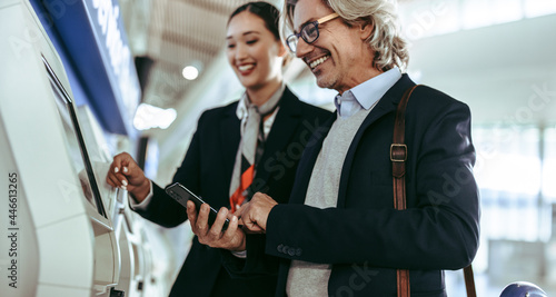 Businessman doing self check in on machine with flight attendant