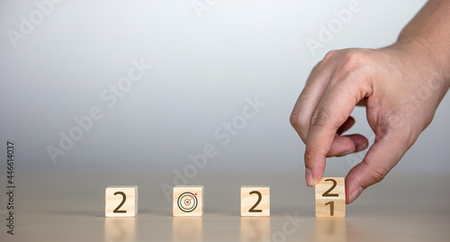 man's hand flipping a wooden block with 2022 message and target board icon on wooden cube. Space for text and designs, copy space. new year concept and setting goals in the starting