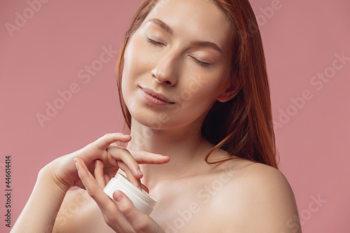 Portrait of young female fashion model isolated on prink studio background. Beautiful caucasian redheaded woman with well-kept skin.