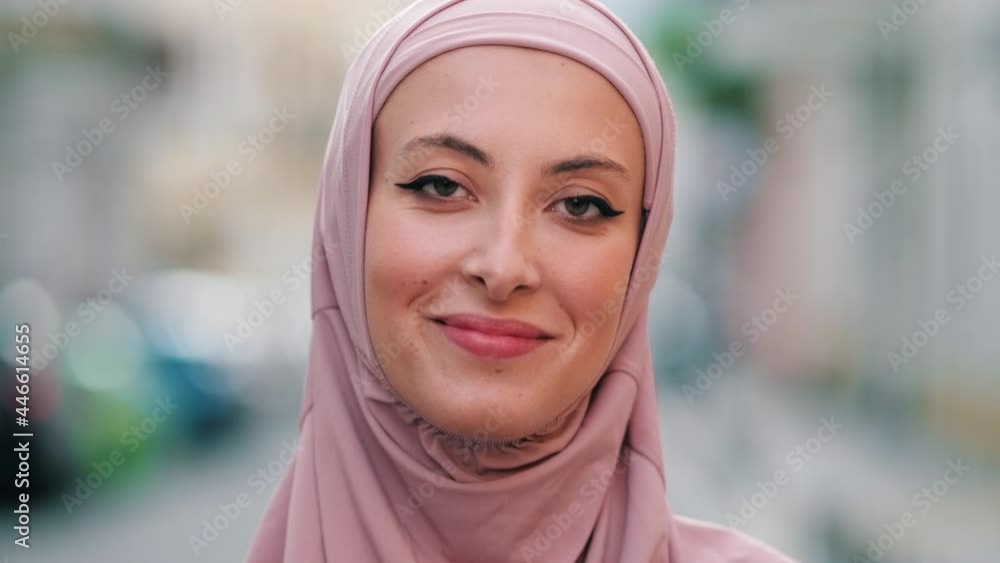 A close-up view of a smiling arabian woman wearing pink national hijab is posing to the camera while standing outside on the street A close-up view of a smiling arabian woman wearing pink national hijab is posing to the camera while standing outside on the street