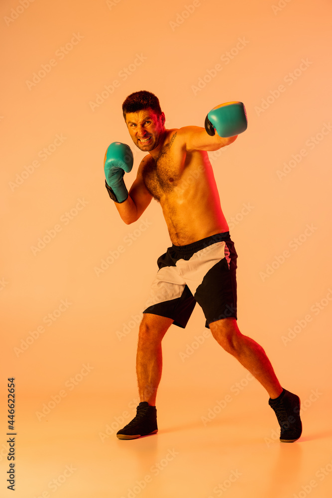 Portrait of Caucasian man, professional boxer in sportwear boxing on studio background in yellow neon light. Concept of sport, activity, movement, wellbeing.