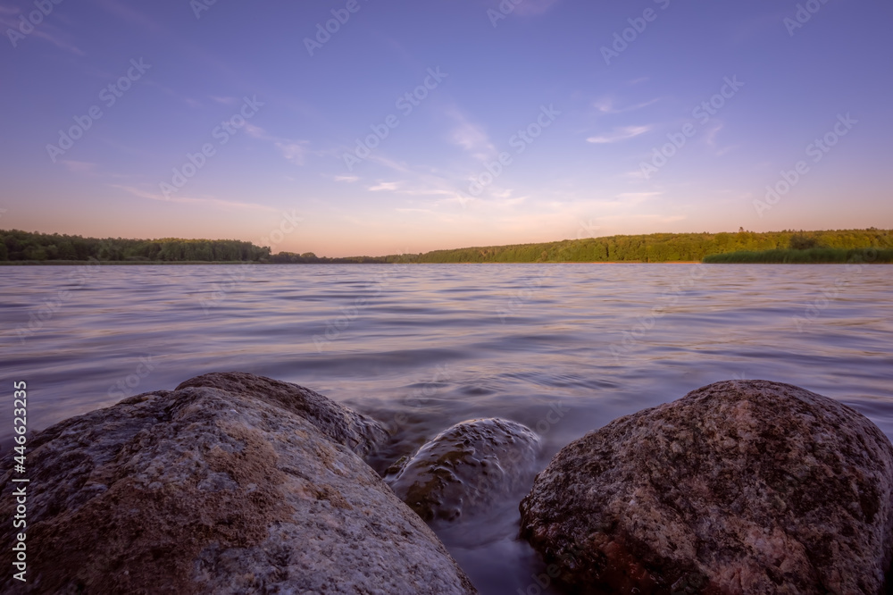 Small boulders submerged in water of a lake on a lakeshore at dusk