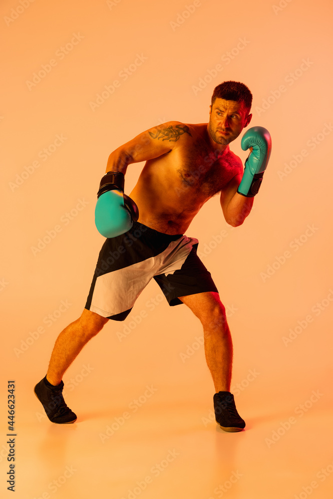 Portrait of Caucasian man, professional boxer in sportwear in action and motion on studio background in yellow neon light. Concept of sport, activity, movement, wellbeing. Portrait of Caucasian man, professional boxer in sportwear in action and motion on studio background in yellow neon light. Concept of sport, activity, movement, wellbeing.