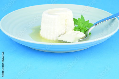 Fresh cheese with honey in circular plate on blue background.