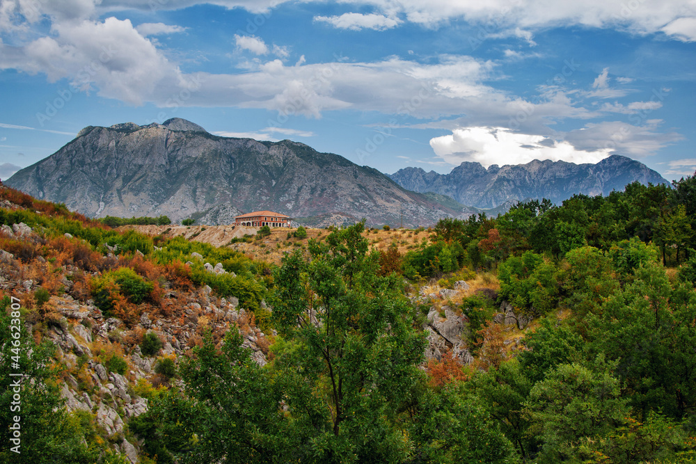 View of canyon in Albanian mountains. Summer landscape with green trees, house on rocky hills and blue sky. View of canyon in Albanian mountains. Summer landscape with green trees, house on rocky hills and blue sky.