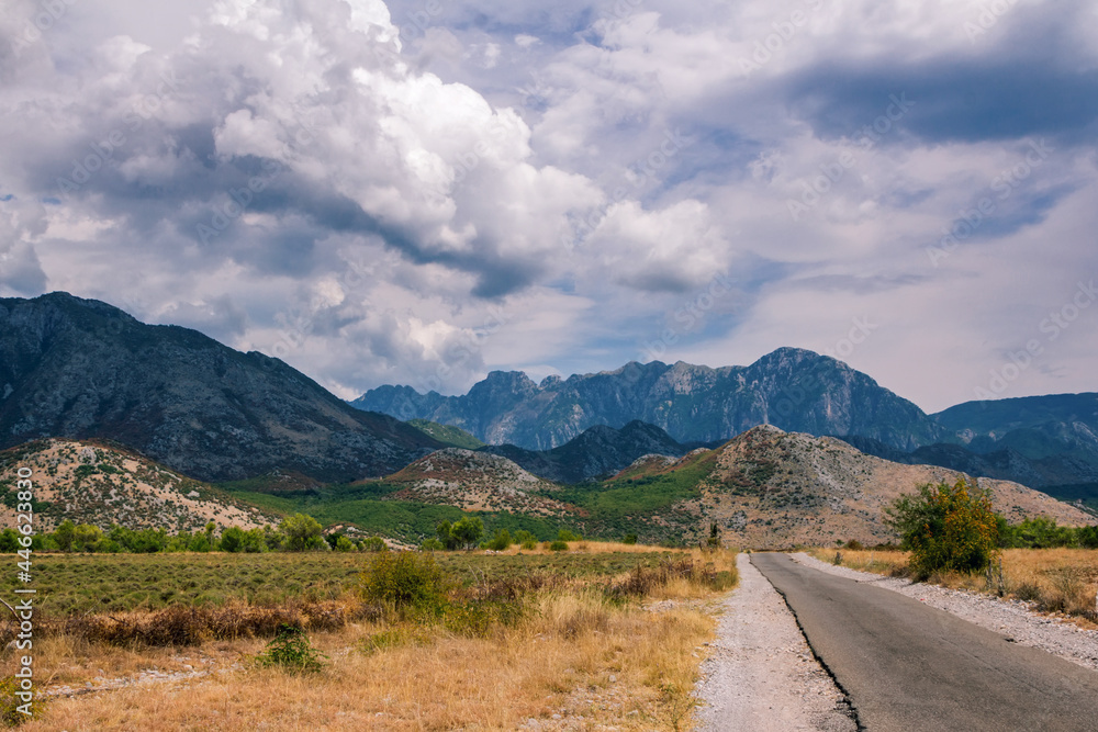 Summer landscape - valley and road in Albanian mountains, agricultural fields and gray clouds on the sky