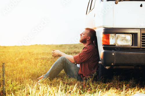Driver in a shirt and jeans sits near his car photo