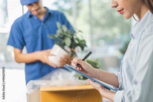 Close up hand of owner business asian woman checking list on clipboard. Cargo company delivery man, male packing, unpacking plant pot in cardboard box. Moving, preparing in new house, relocation.