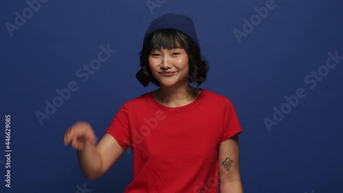 A smiling asian woman is doing looser gesture standing isolated over blue wall in the studio photo