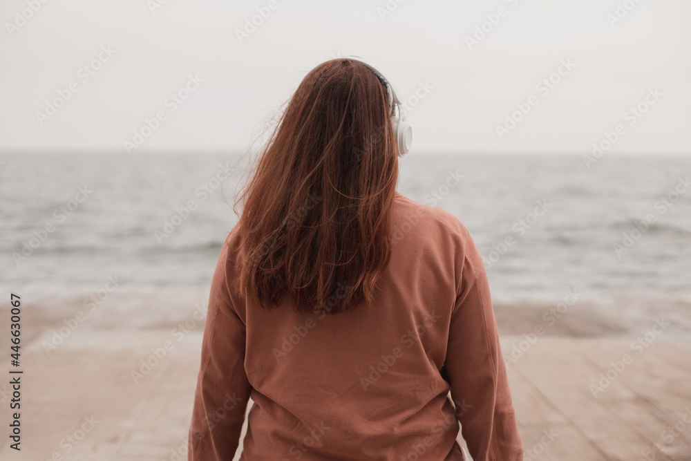 Women with headphones on the beach near the sea, back view Women with headphones on the beach near the sea, back view