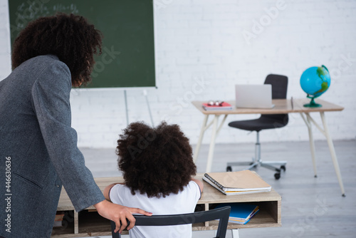 African american teacher standing near pupil in classroom
