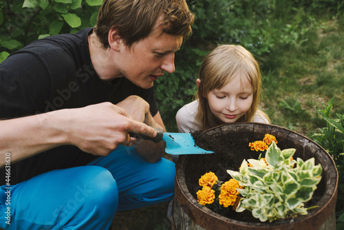 the priest shows his daughter how to plant flowers in the garden and digs the ground with a spatula