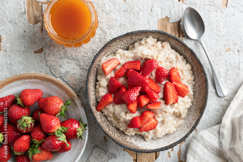 Oatmeal porridge bowl with strawberries and honey on concrete background, table top view. Clean eating, dieting concept photo