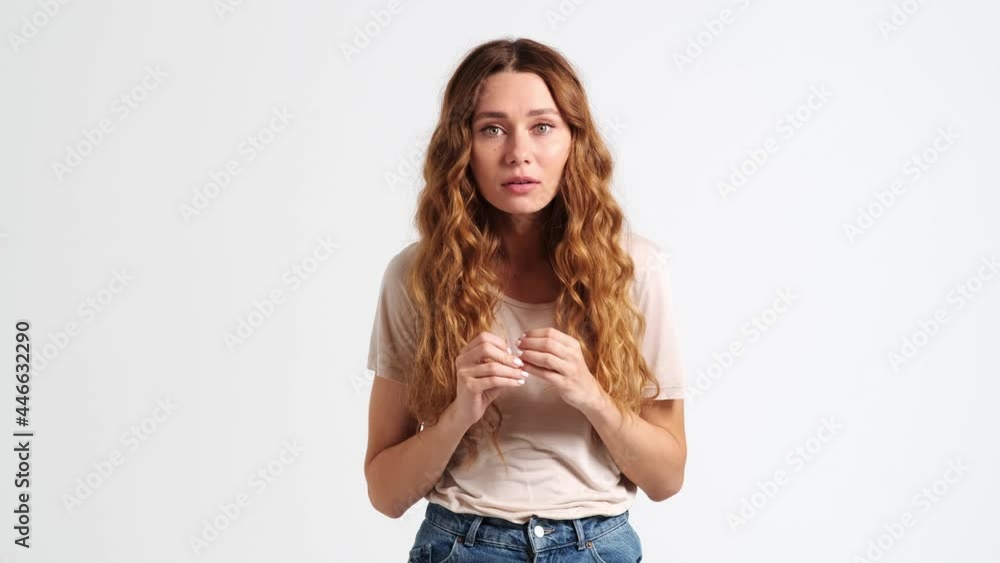 A frightened shocked woman is looking to the camera standing isolated over a white wall in the studio A frightened shocked woman is looking to the camera standing isolated over a white wall in the studio