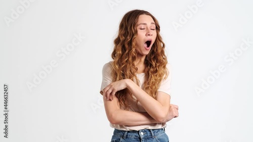 A bored woman is yawning standing isolated over a white wall in the studio