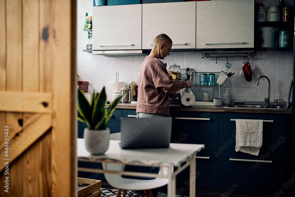 A beautiful senior woman standing in a kitchen and preparing tea or morning coffee.