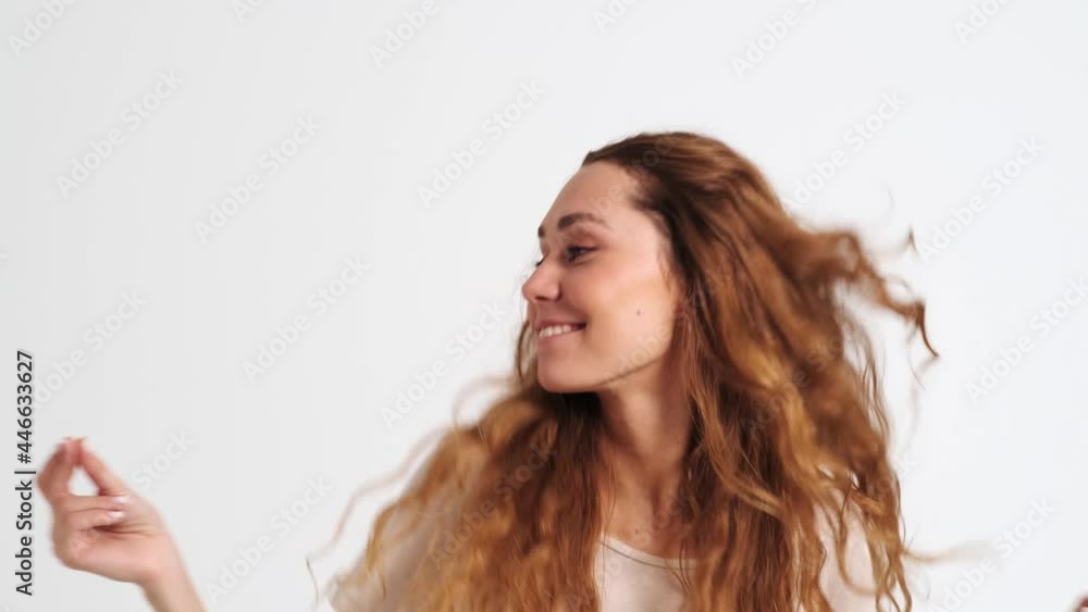 A happy woman is shaking her hair standing isolated over a white wall in the studio A happy woman is shaking her hair standing isolated over a white wall in the studio
