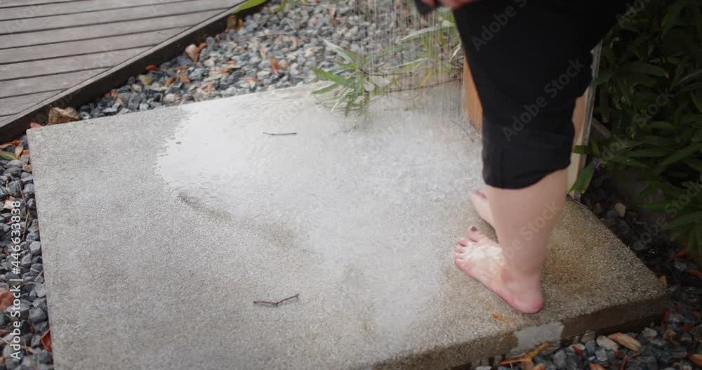 Young woman washing cleaning legs feet under the tap at outdoor shower in summertime