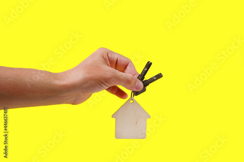 House keys with a keychain in hand on a yellow background.