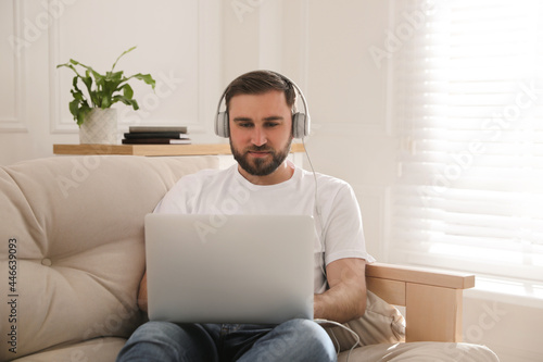 Man with laptop and headphones sitting on sofa at home