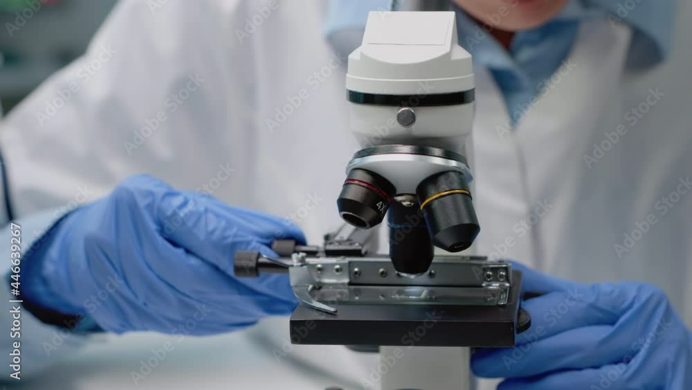 Close up of scientific microscope in laboratory and specialist hands using lens with magnifying glass for dna test and analysis. Doctor with gloves analyzing sample for investigation Close up of scientific microscope in laboratory and specialist hands using lens with magnifying glass for dna test and analysis. Doctor with gloves analyzing sample for investigation