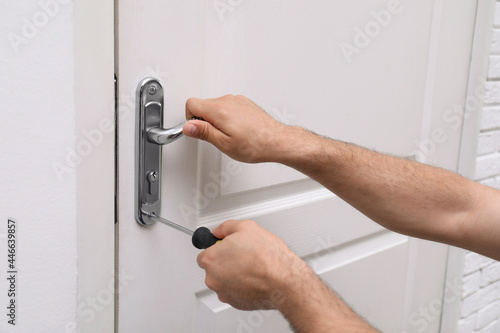 Handyman with screwdriver repairing door lock indoors, closeup