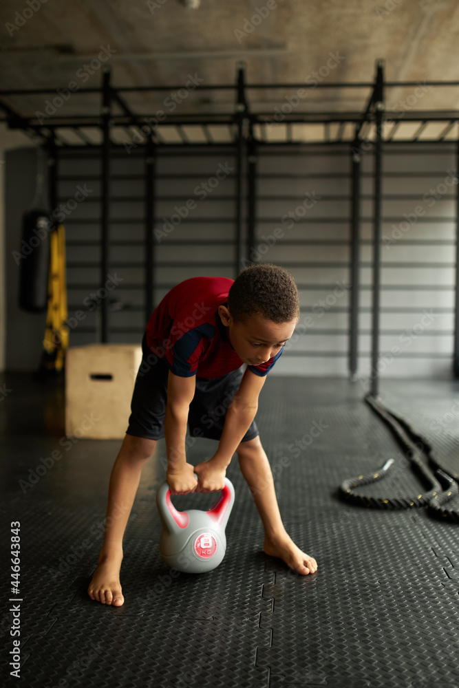 Naklejka premium Kid get ready to lift heavy dumbbell, preparing for exercise, watch posture and breathing. Work hard to become successful sportsman in future. Goal, dream, career, sport concept