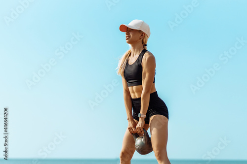 Sportswoman in sportswear lifting weights, Sportive woman holding a kettlebell during crossfit workout, on the beach