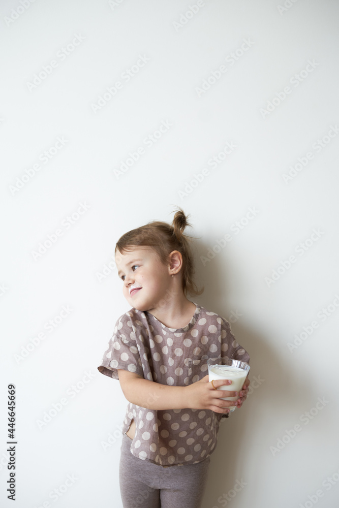 a little girl with tails against a white wall is standing in her hands holding a glass of kefir dissatisfied a little girl with tails against a white wall is standing in her hands holding a glass of kefir dissatisfied