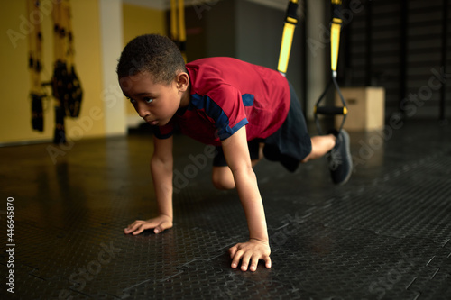 Latino american schoolboy perform exercise using gym equipment, train legs on special belts. Set goal and go for it. Never give up, sport, athlete, active lifestyle, childhood concept