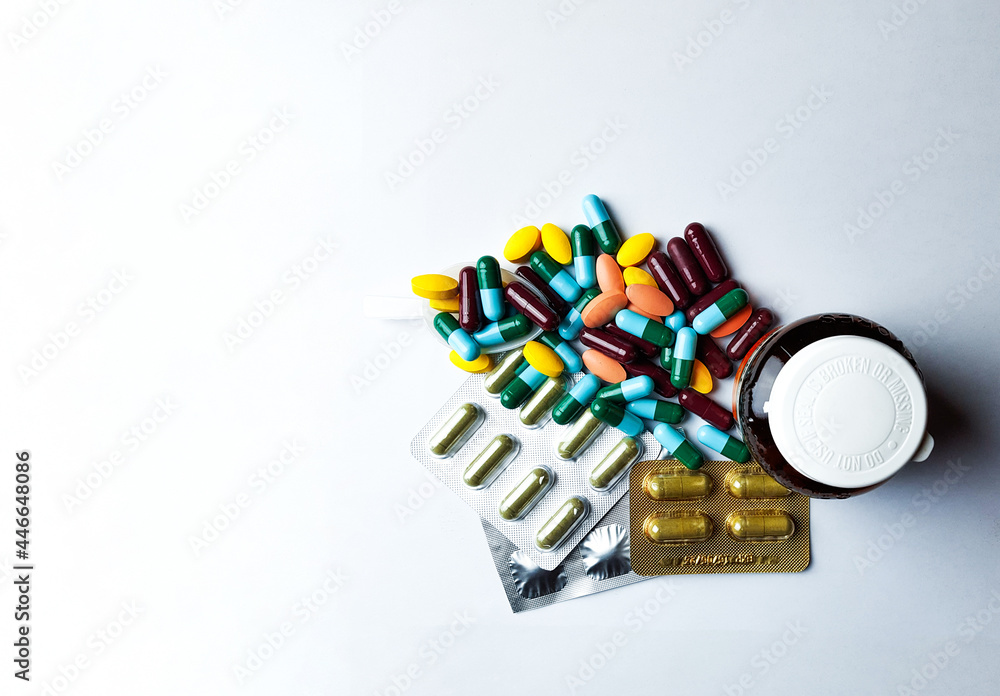 Assort pharmaceutical medicine pills, orange tablets, blue and green capsules with bottle on white background, soft and selective focus Assort pharmaceutical medicine pills, orange tablets, blue and green capsules with bottle on white background, soft and selective focus