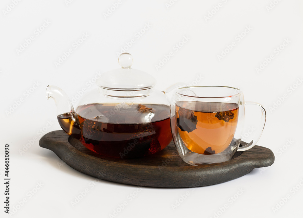 Chaga mushroom infusion on a white background. Chaga drink in a glass teapot and a cup on a wooden tray. Trendy healthy drink. Chaga mushroom infusion on a white background. Chaga drink in a glass teapot and a cup on a wooden tray. Trendy healthy drink.
