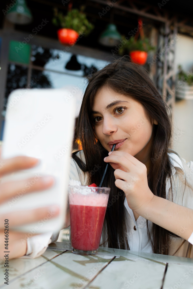 young woman sitting in a coffee shop drinking a milkshake while taking a selfie young woman sitting in a coffee shop drinking a milkshake while taking a selfie