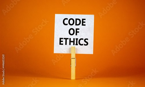 Code of ethics symbol. White paper with words 'Code of ethics', clip on wood clothespin. Beautiful orange background. Business and code of ethics concept. Copy space.