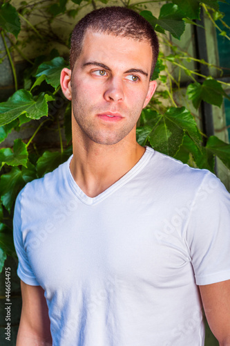 Portrait of a young man, wearing a white V-neck T-shirt, short hair. The background is green ivy leaves. Close Up..