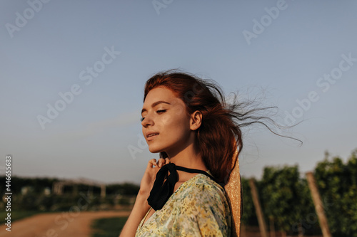 Charming woman with ginger hairstyle, cute freckles and dark bandage on neck in green and yellow modern clothes posing outdoor. .