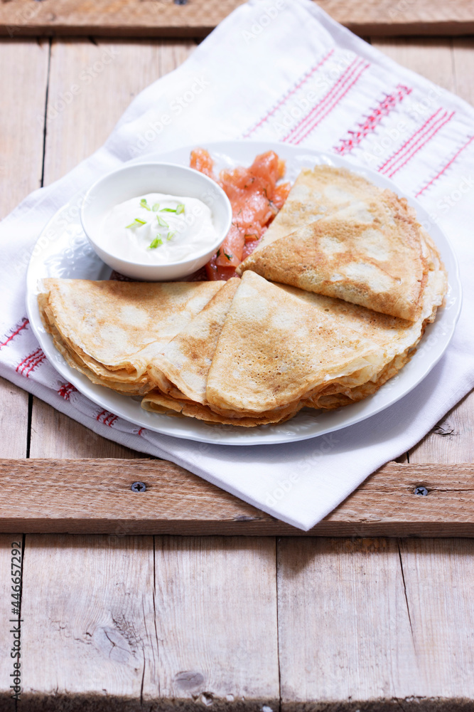 Thin pancakes with salmon and sour cream on a light background. Rustic style.
