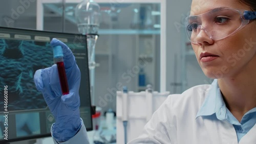 Close up of scientist analyzing lab vacutainer with fluid in laboratory. Woman with chemical equipment holding glass flask for blood cell examination. Transparent tube with solution photo