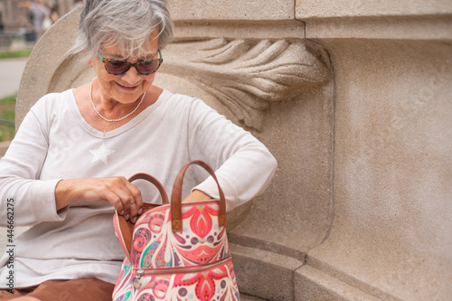 Happy casual senior woman sitting in the park searching for something in her bag. photo