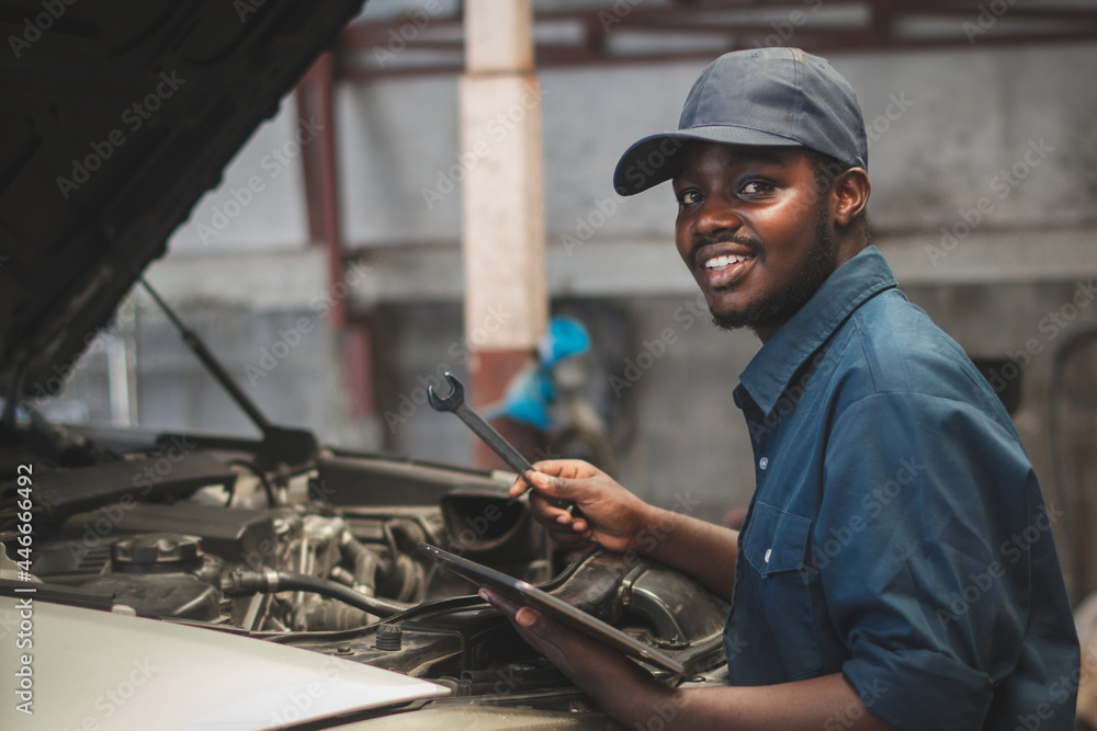 African maintenance male checking car with use wrench and tablet , service via insurance system at Auomobile repair and check up center