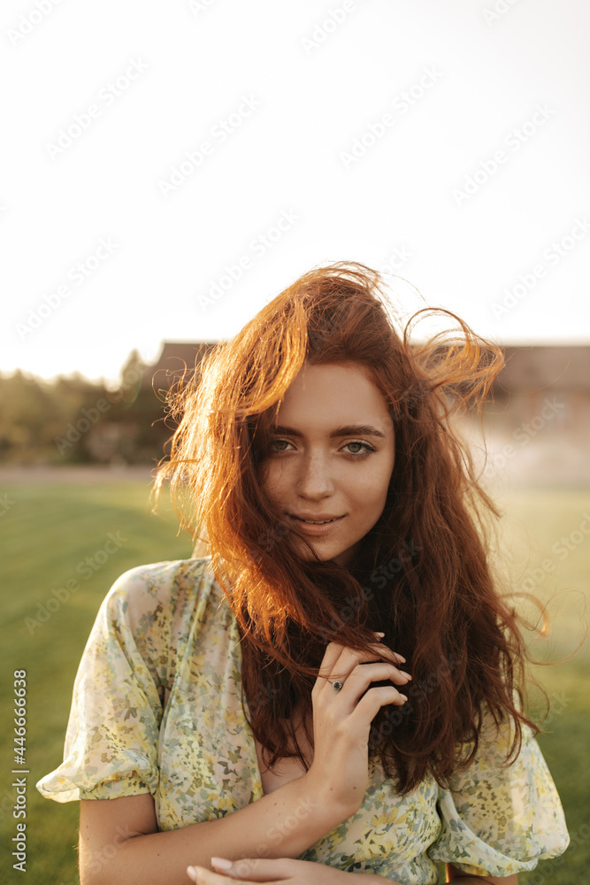 Tender lady with foxy long hairstyle and cute freckles in modern cool green dress smiling and looking into camera outdoor.. Tender lady with foxy long hairstyle and cute freckles in modern cool green dress smiling and looking into camera outdoor..
